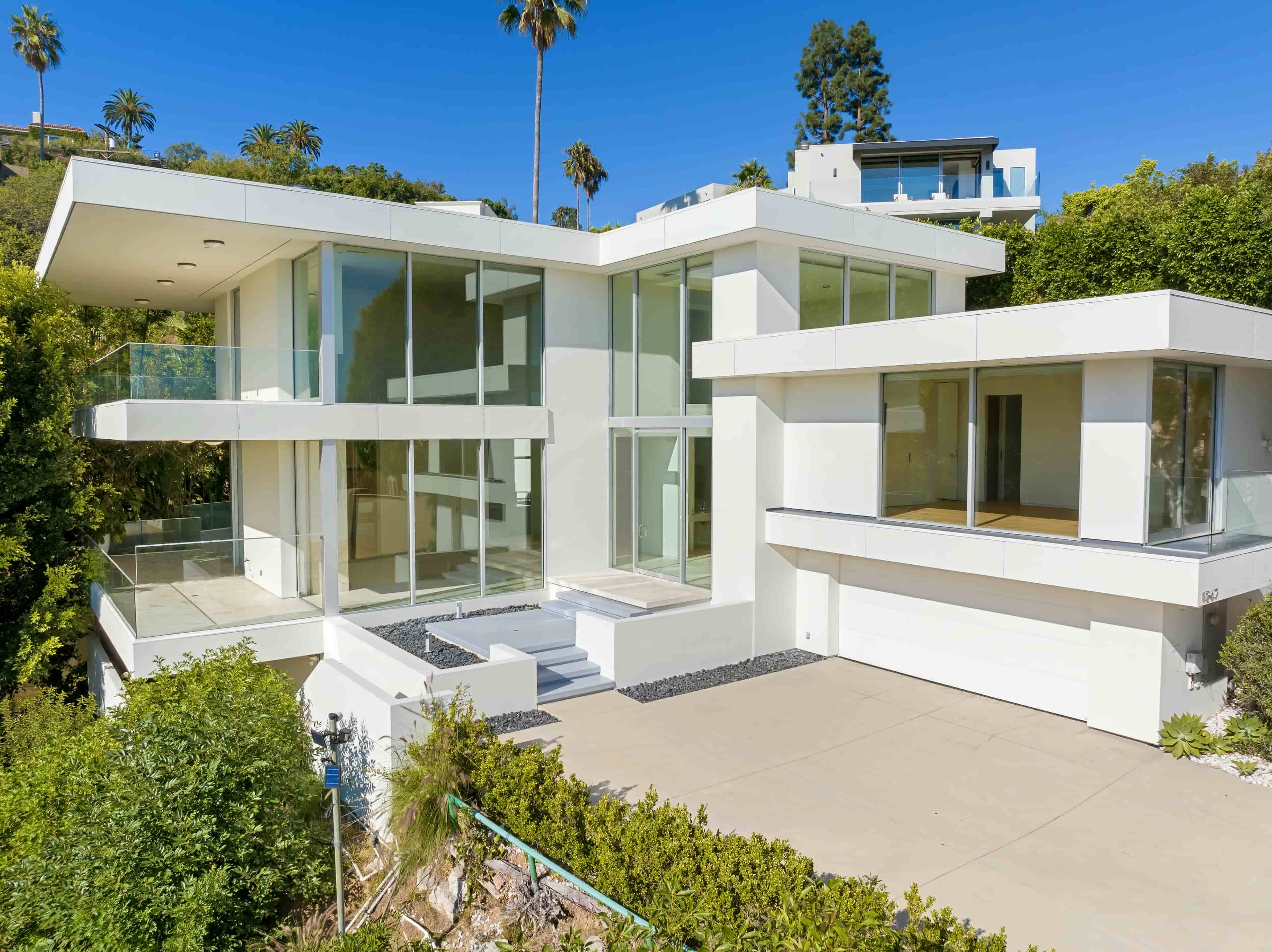 Modern white glass hillside mansion with palm trees